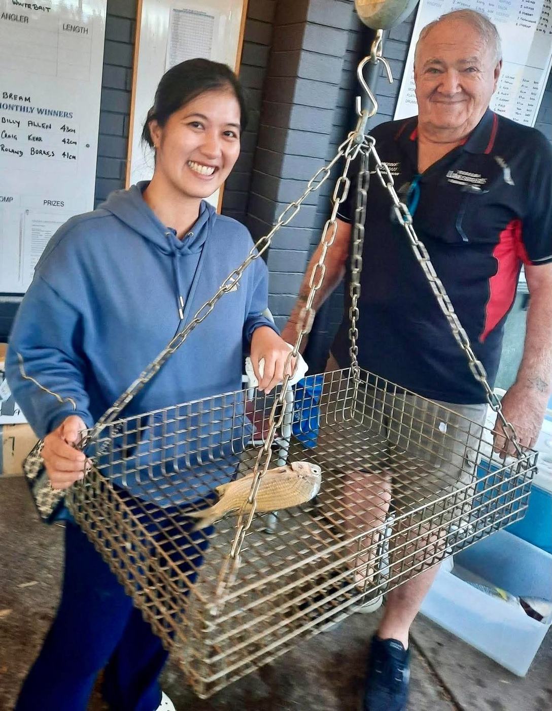 A woman angler and a club official weighing a whiting in the hanging basket